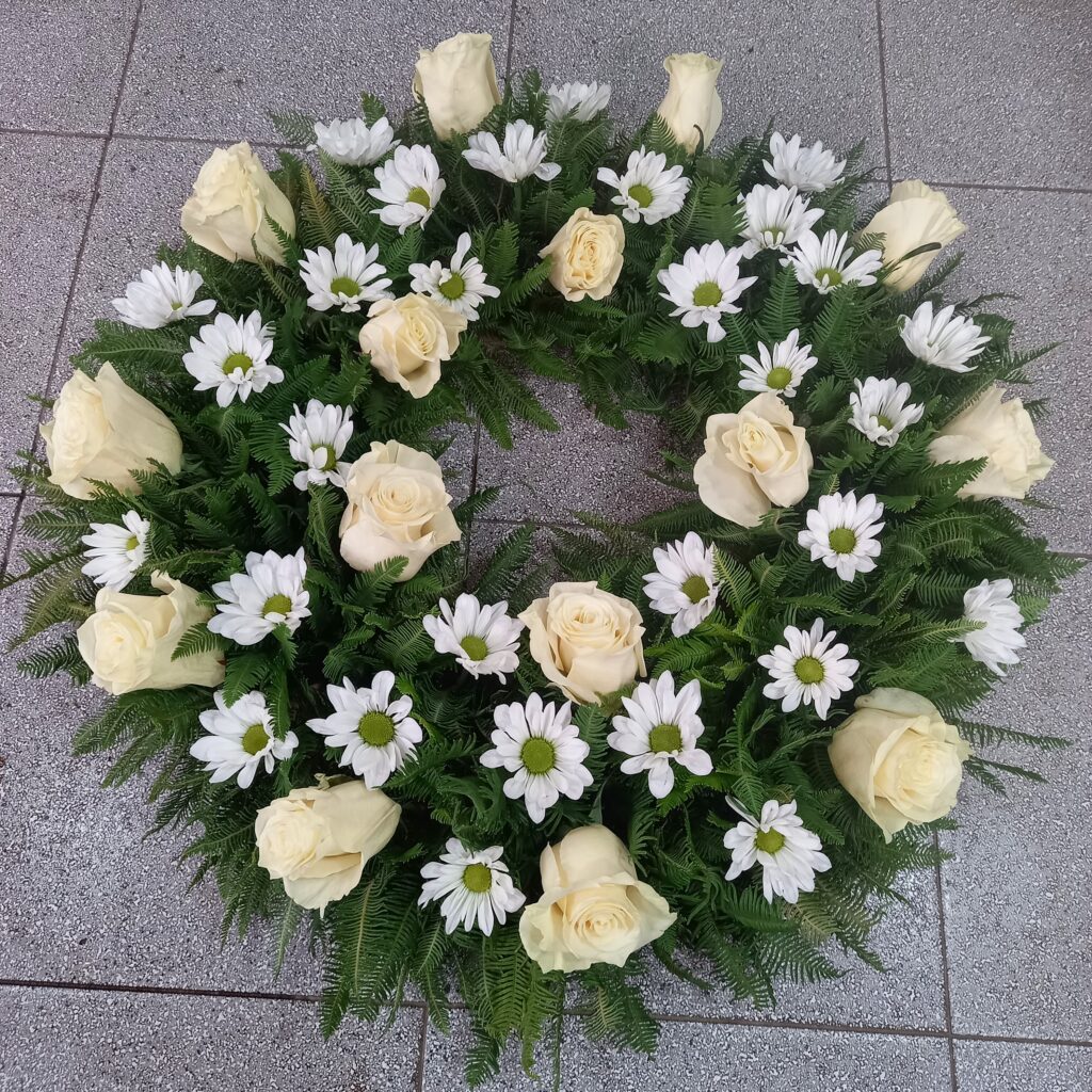 Corona de flores blancas compuesta por rosas, margaritas y helechos