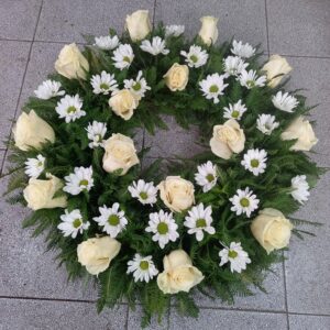 Corona de flores blancas compuesta por rosas, margaritas y helechos
